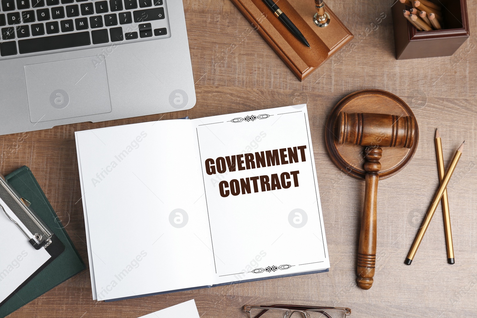 Image of Notebook with words Government Contract on wooden table. Workplace with laptop, stationery and gavel, flat lay