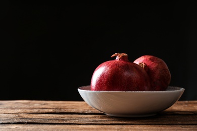 Photo of Plate with ripe pomegranates on table against black background, space for text