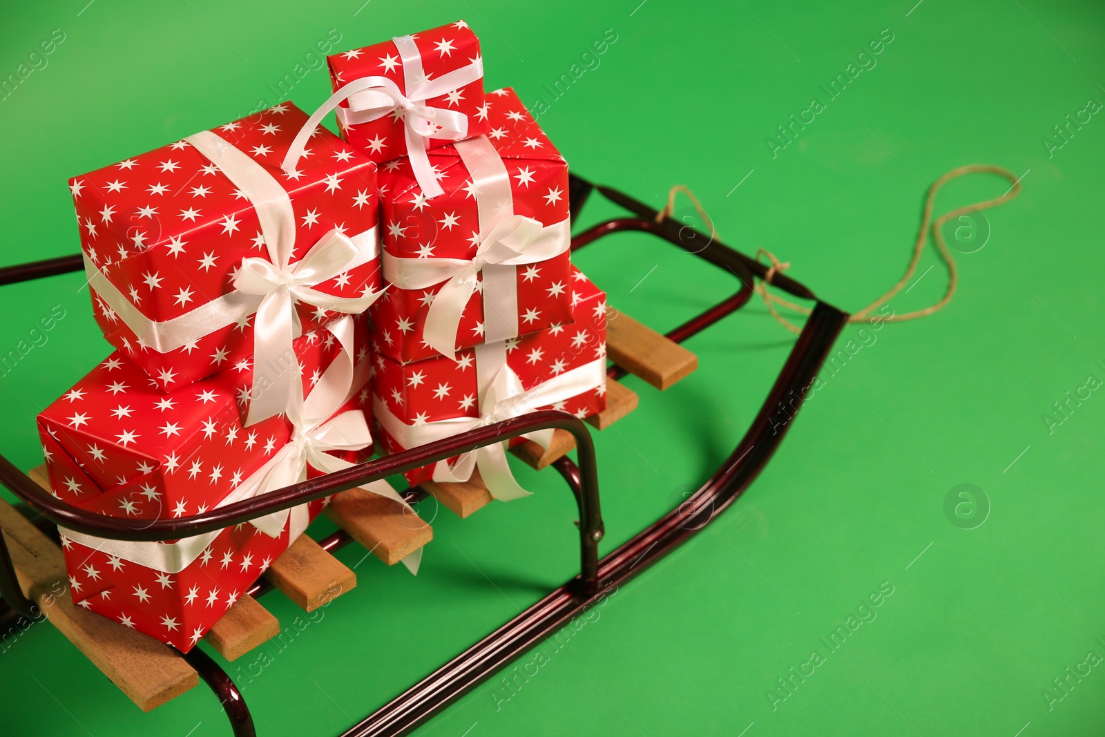 Photo of Sleigh with gift boxes on green background, closeup