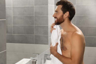 Photo of Handsome man with towel in front of mirror in bathroom