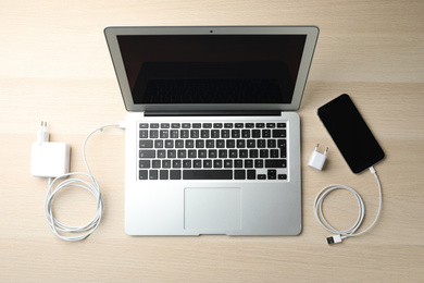 Photo of Chargers, smartphone and laptop on wooden table, flat lay. Modern technology