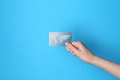 Woman holding credit card on light blue background, closeup