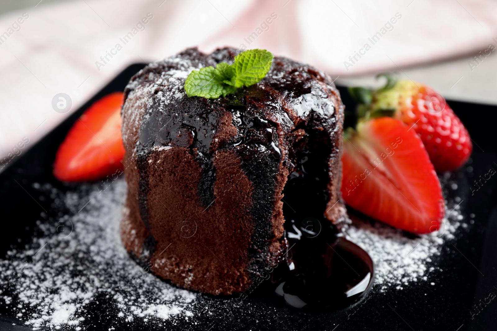 Photo of Delicious warm chocolate lava cake with mint and strawberries on plate, closeup