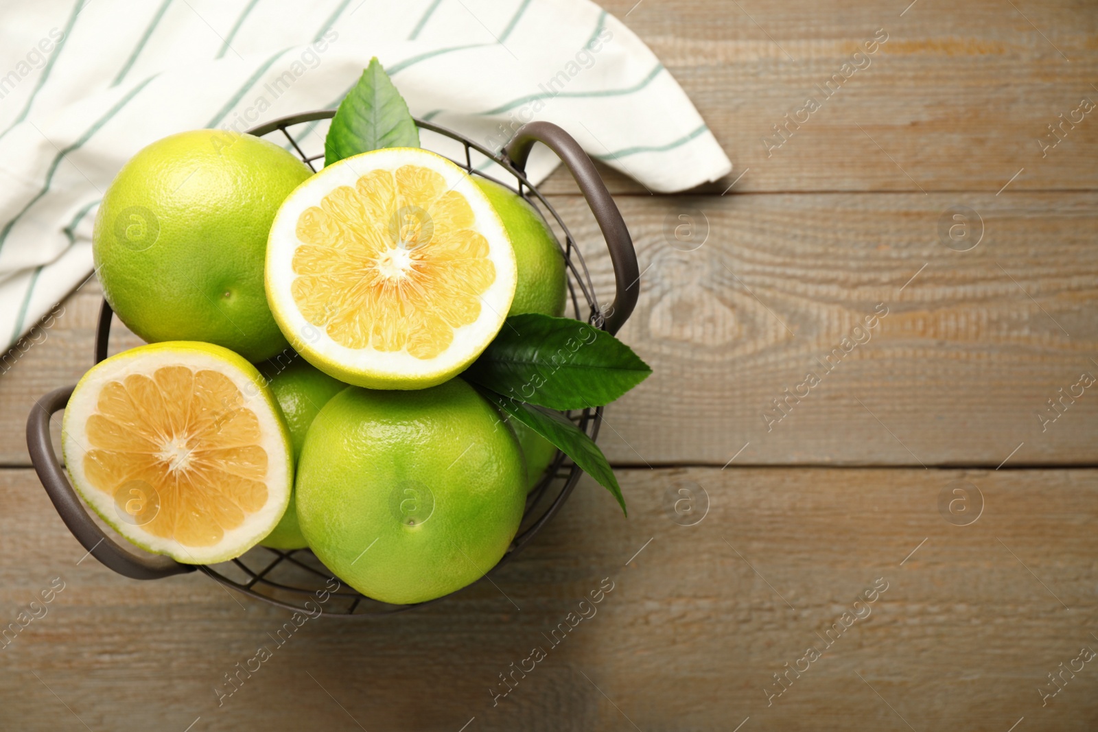 Photo of Whole and cut sweetie fruits in metal basket on wooden table, flat lay. Space for text