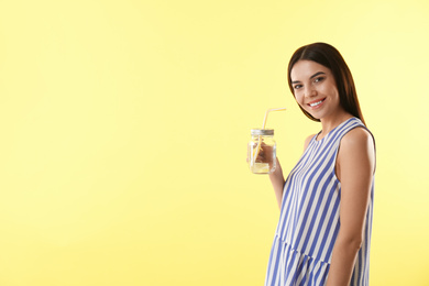 Beautiful young woman with tasty lemon water on yellow background. Space for text