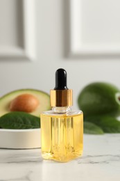 Photo of Bottle of essential oil and avocados on white marble table