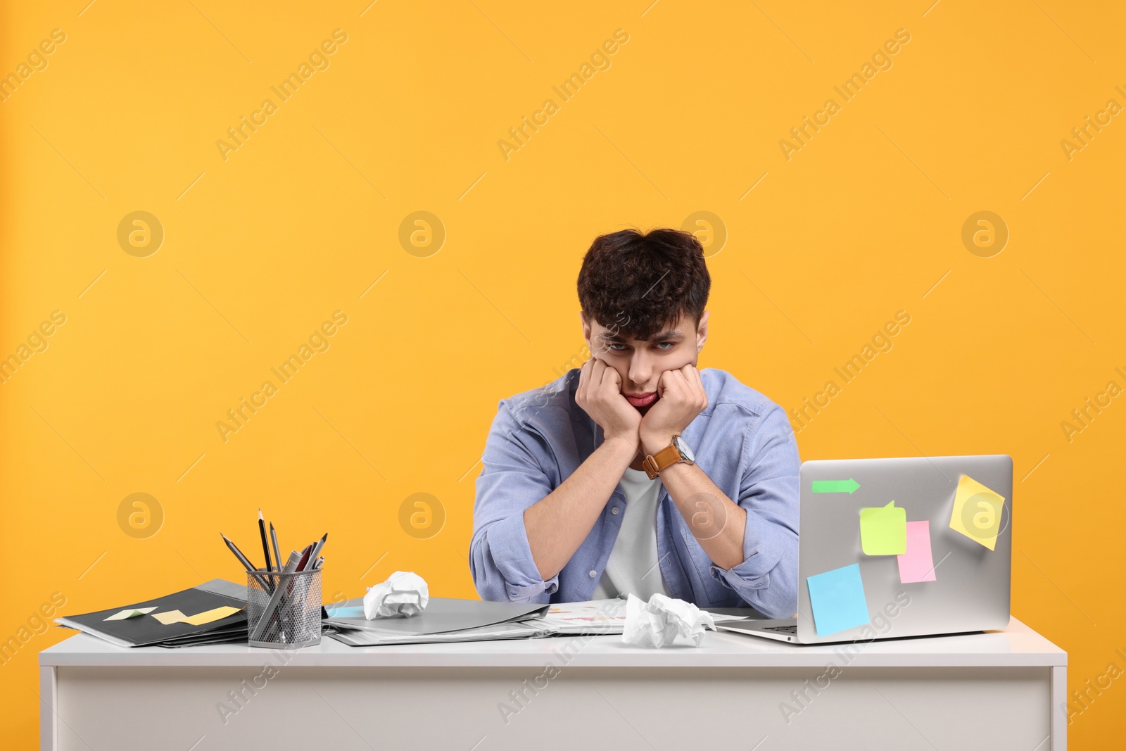 Photo of Tired young man working at white table on orange background. Deadline concept