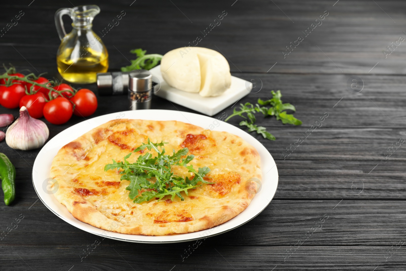 Photo of Delicious khachapuri with cheese, arugula, spices and vegetables on dark wooden table