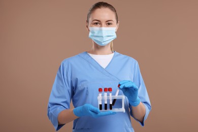 Laboratory testing. Doctor with blood samples in tubes on light brown background