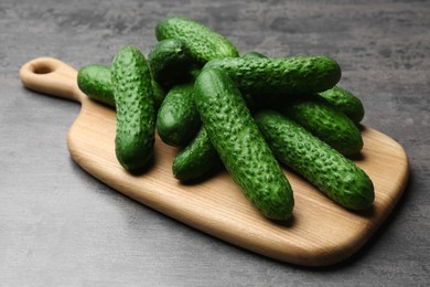 Photo of Wooden board with fresh ripe cucumbers on dark grey table