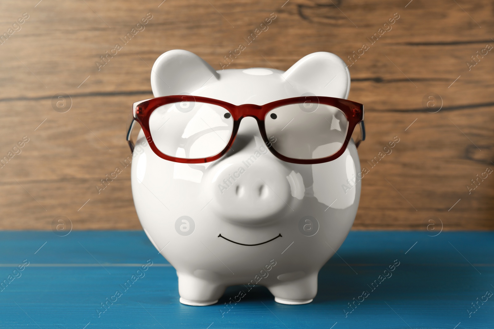 Photo of Ceramic piggy bank with glasses on blue wooden table