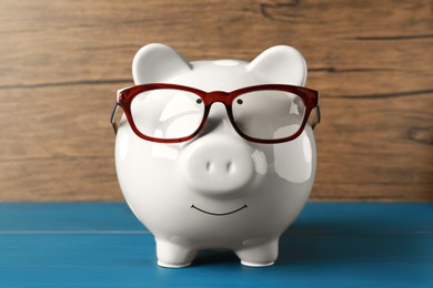 Photo of Ceramic piggy bank with glasses on blue wooden table