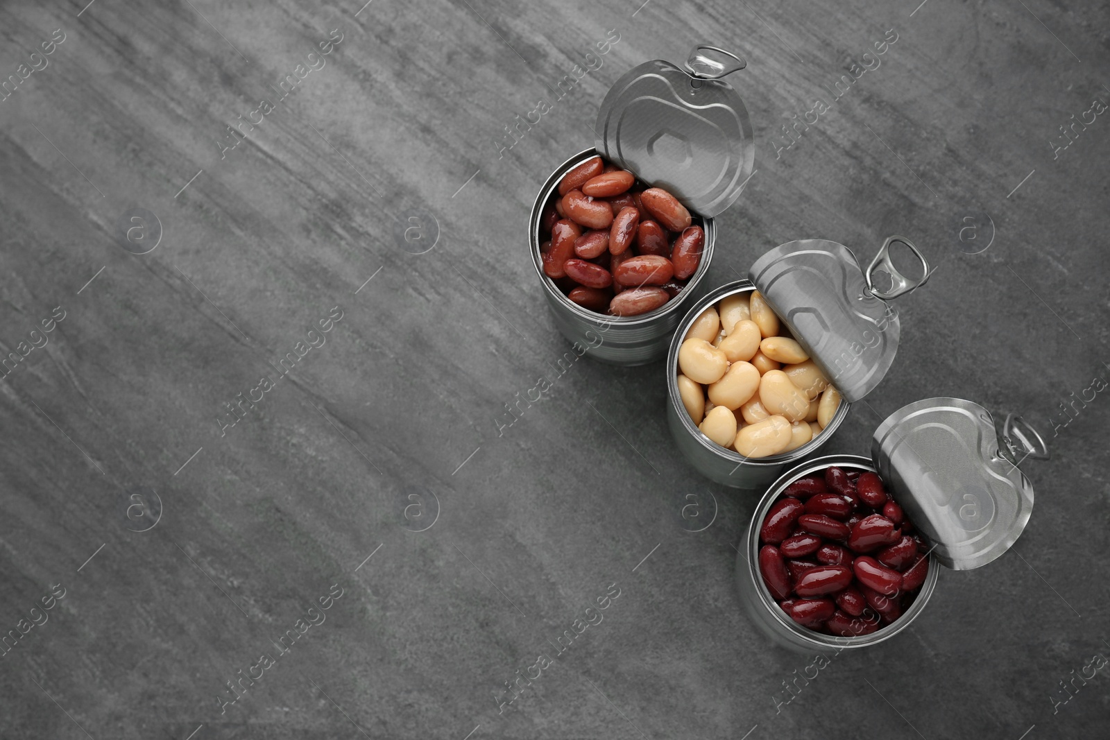 Photo of Tin cans with different canned kidney beans on grey table, flat lay. Space for text