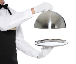 Young waiter holding metal tray with lid on white background