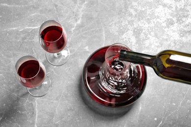 Pouring delicious red wine into decanter on grey table, above view