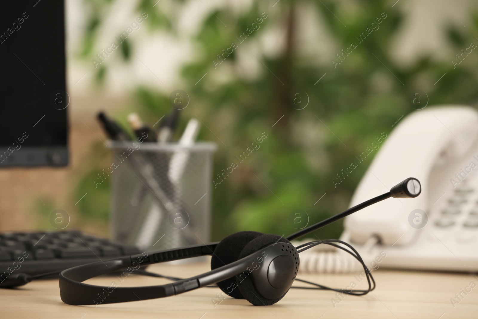 Photo of Headset, desktop telephone and computer on table indoors, space for text. Hotline concept