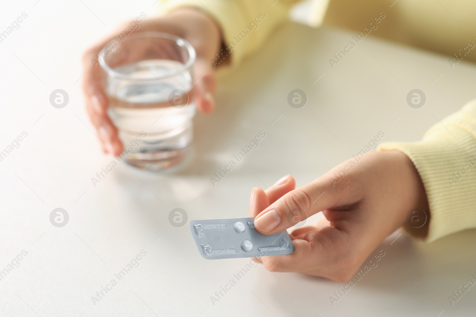 Photo of Woman taking emergency contraception pill at white table indoors, closeup