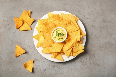 Photo of Plate with delicious mexican nachos chips and cheese sauce on grey table, flat lay