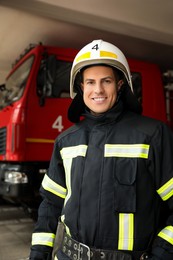 Photo of Portrait of firefighter in uniform and helmet near fire truck at station