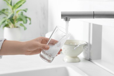 Woman filling glass with water from tap in kitchen, closeup