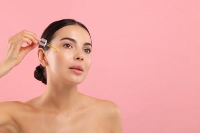 Photo of Beautiful young woman applying serum onto her face on pink background. Space for text