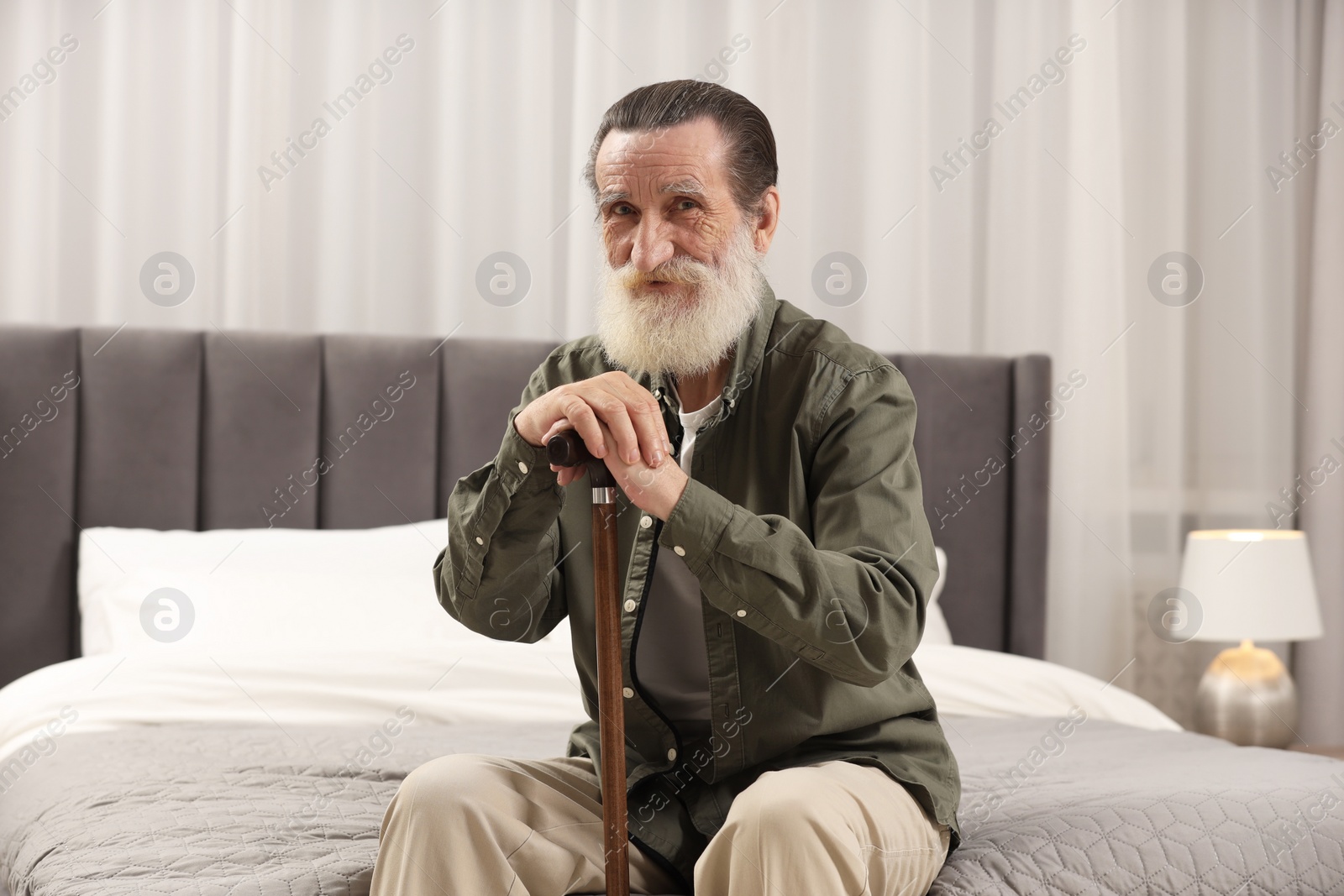 Photo of Senior man with walking cane on bed at home