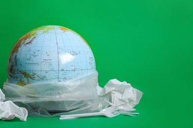 Photo of Globe in plastic bag and garbage on green background, space for text. Environmental conservation