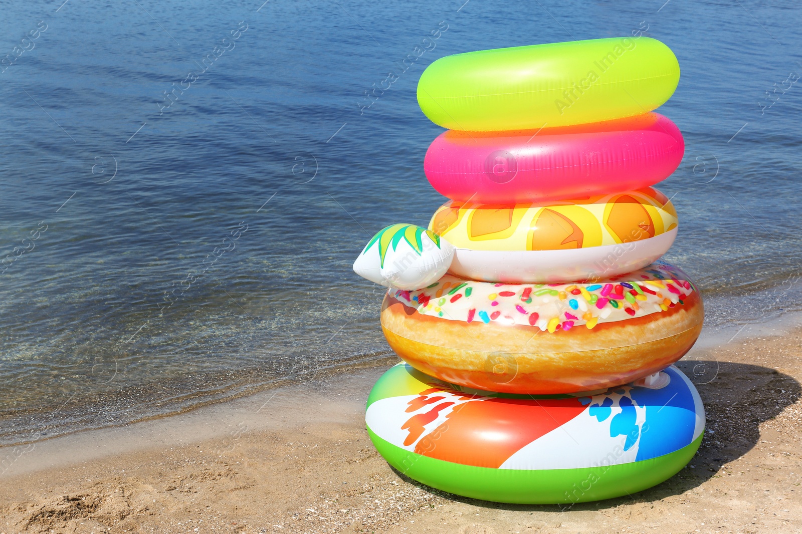 Photo of Stack of different bright inflatable rings on sandy beach near sea. Space for text