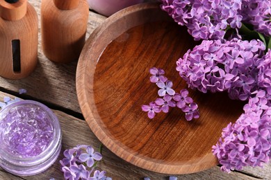 Photo of Bowl with water, lilac flowers and cosmetic products on wooden table, above view