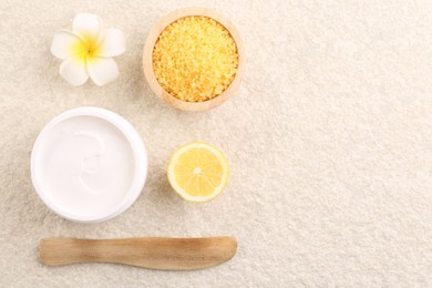 Flat lay composition with moisturizing cream in open jar and other body care products on light textured table. Space for text