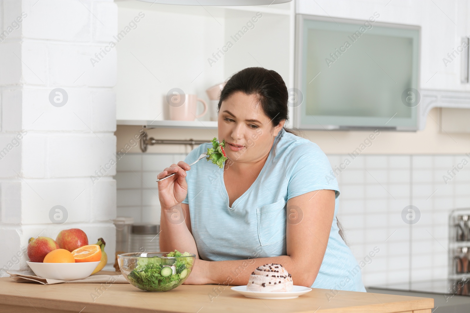 Photo of Woman choosing between vegetable salad and dessert in kitchen. Healthy diet