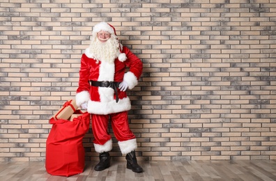 Authentic Santa Claus with big red bag full of gifts near brick wall