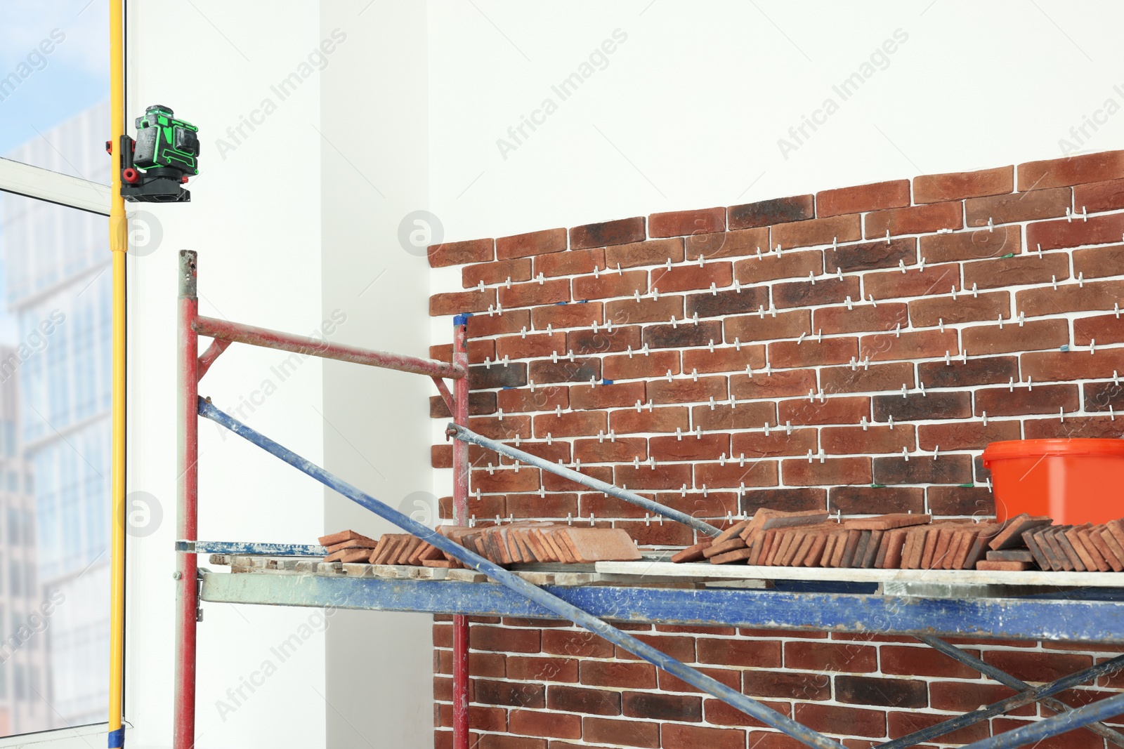 Photo of Scaffolding near wall with decorative bricks and tile leveling system indoors