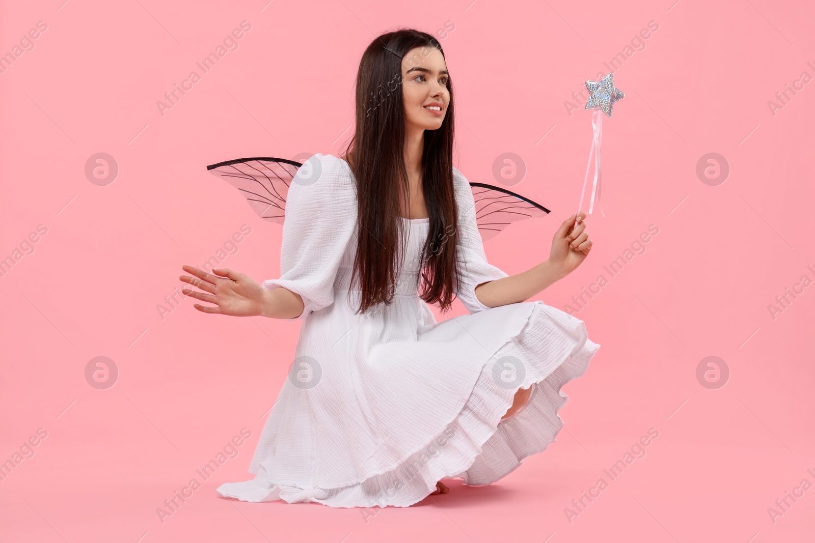 Photo of Beautiful girl in fairy costume with wings and magic wand on pink background