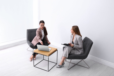 Photo of Young businesswomen sitting in armchairs at table indoors