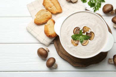 Photo of Delicious homemade mushroom soup in ceramic pot, croutons, fresh champignons and parsley on white wooden table, flat lay