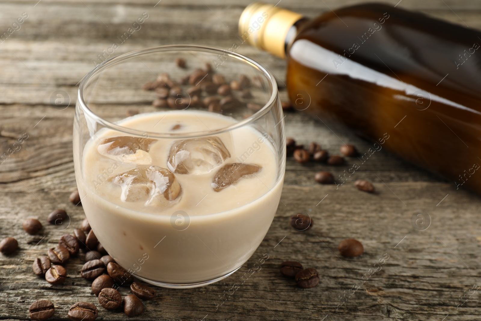 Photo of Coffee cream liqueur in glass, beans and bottle on wooden table, closeup
