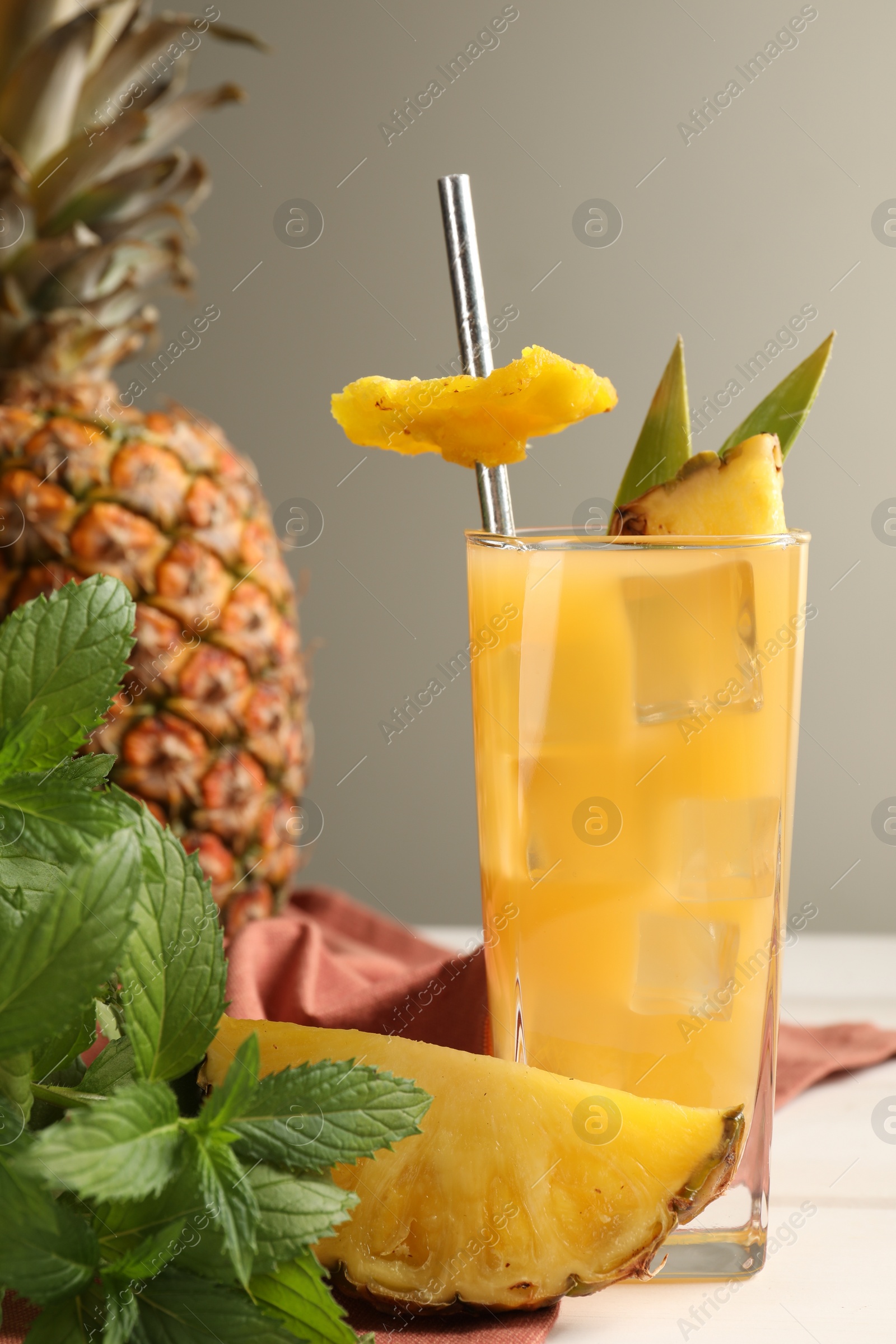 Photo of Glass of tasty pineapple cocktail, fresh fruit and mint on white table