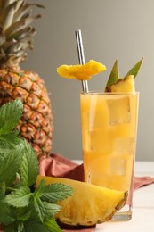 Photo of Glass of tasty pineapple cocktail, fresh fruit and mint on white table