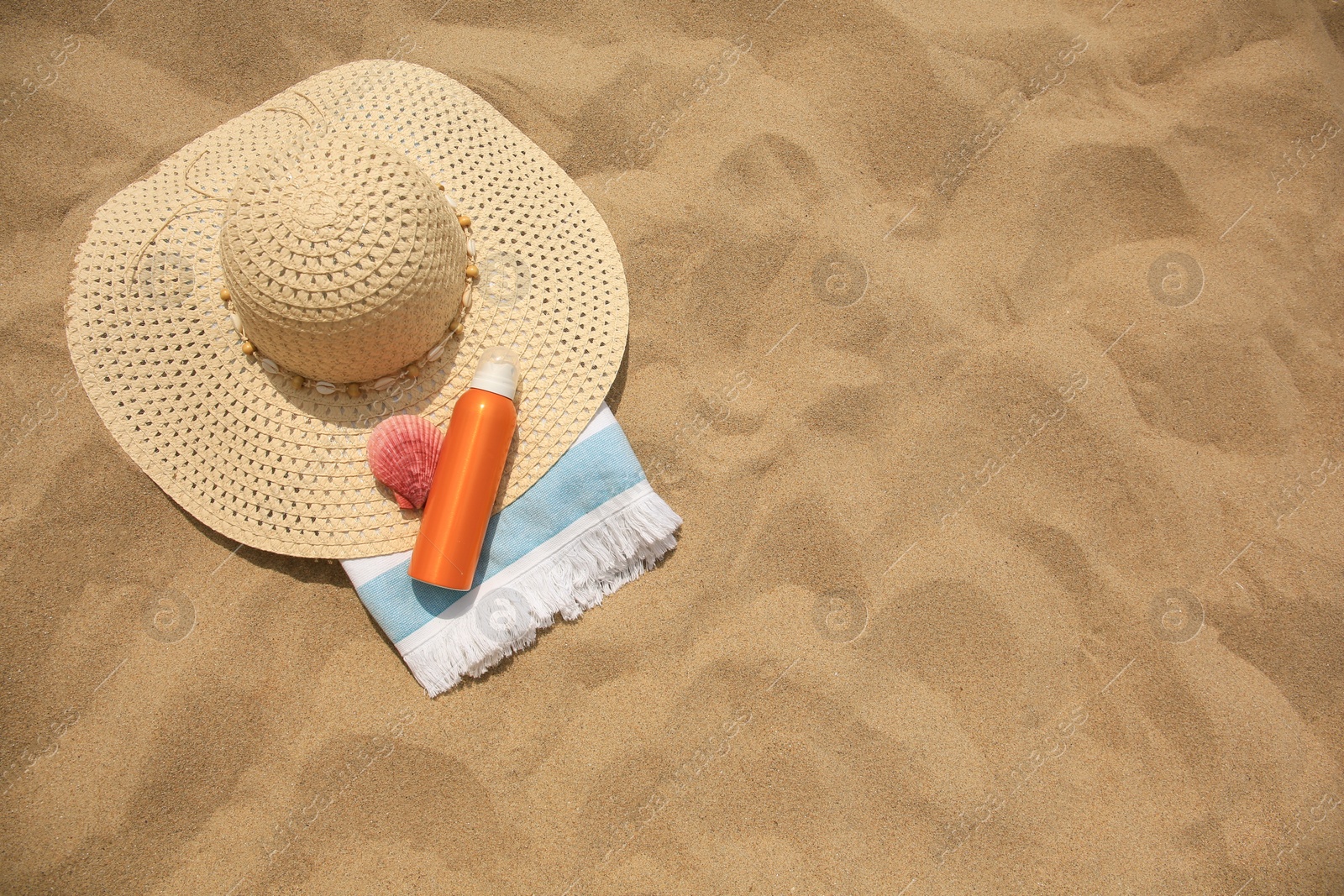 Photo of Sunscreen, hat, seashell and towel on sand, flat lay with space for text. Sun protection care