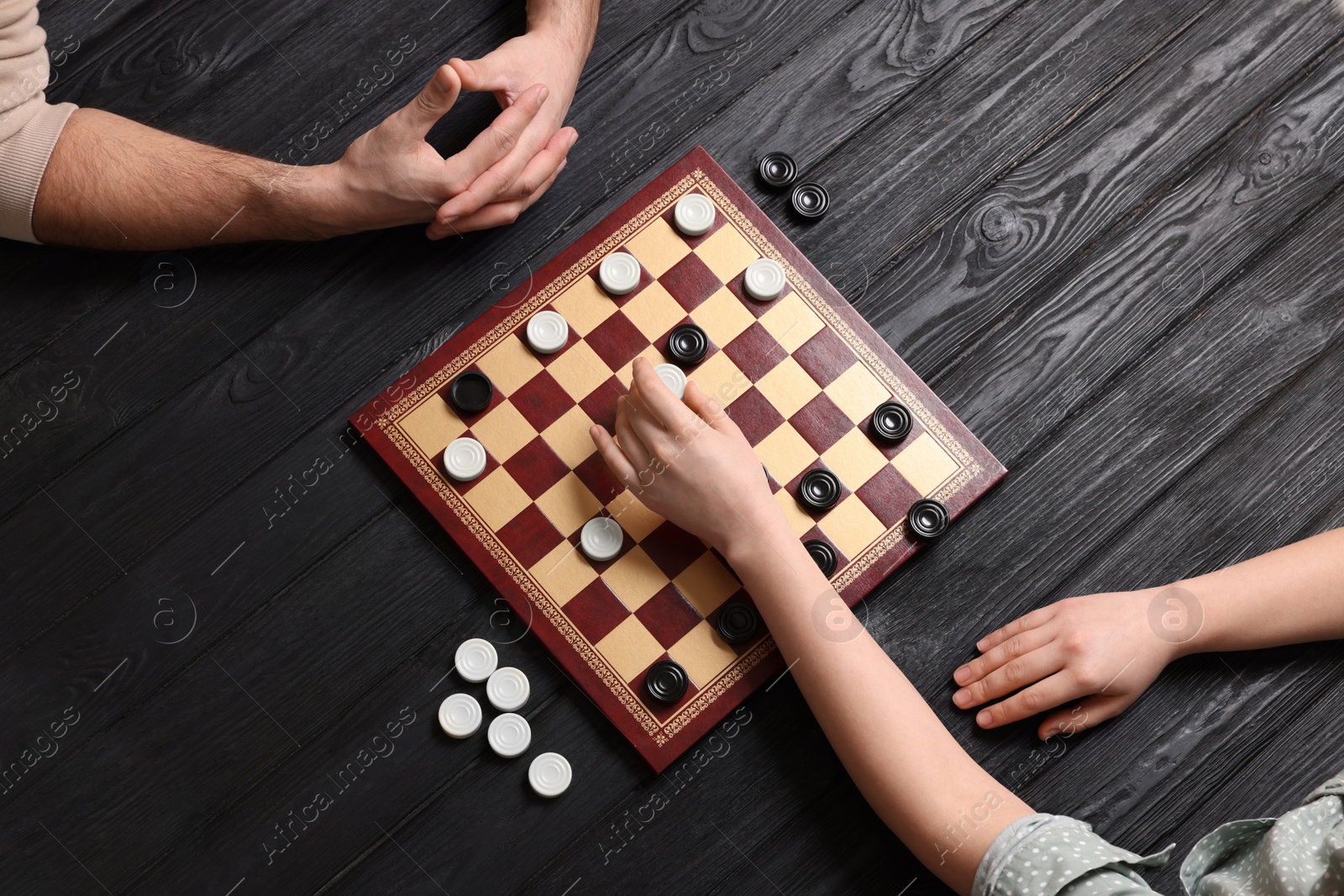 Photo of Man playing checkers with woman at black wooden table, top view