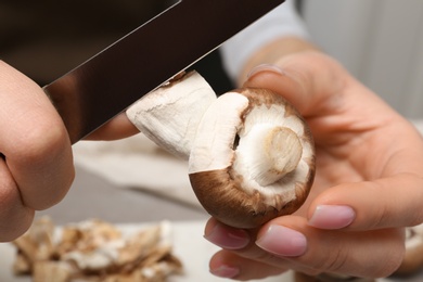 Photo of Young woman peeling fresh champignon mushrooms at table, closeup view