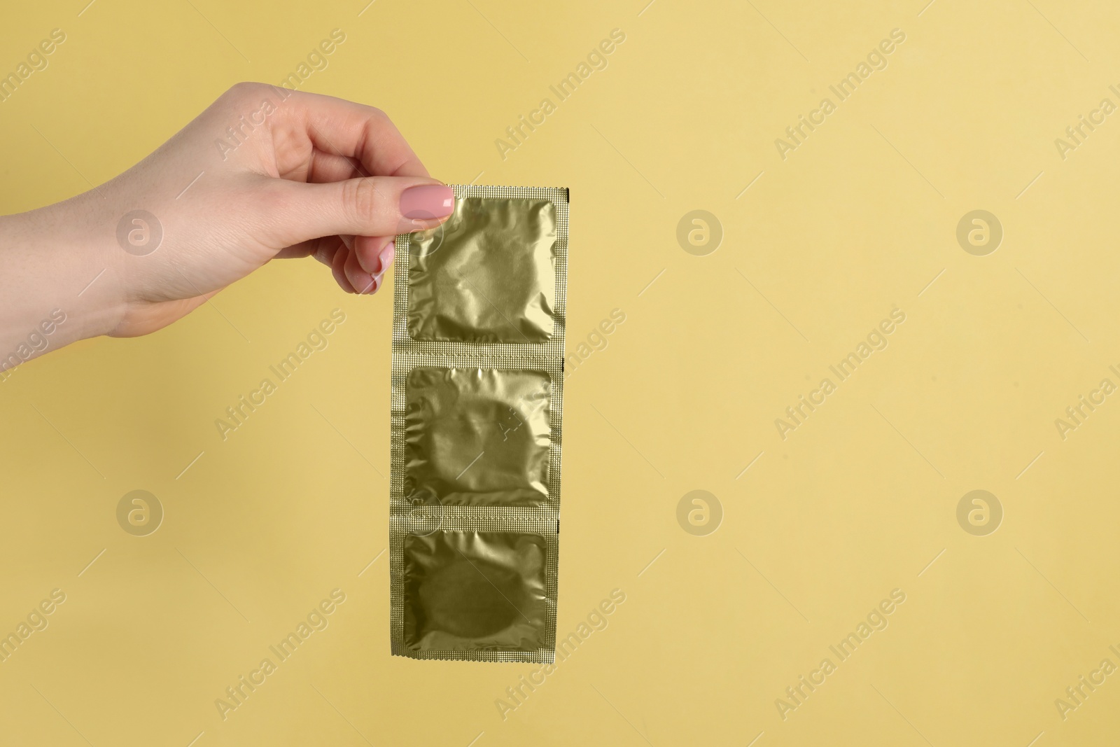 Photo of Woman holding condoms on pale yellow background, closeup. Space for text