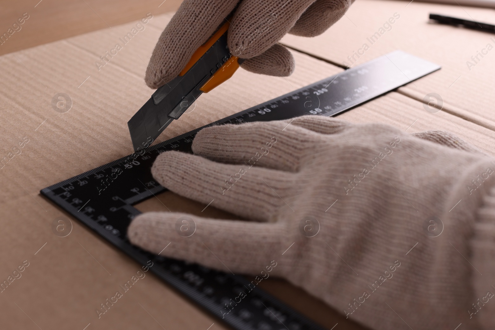 Photo of Worker cutting cardboard with utility knife and ruler, closeup