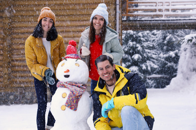 Photo of Happy friends with snowman outdoors on snowy day. Winter vacation