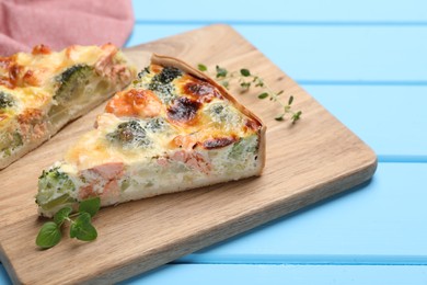 Photo of Pieces of delicious homemade quiche with salmon and broccoli on light blue wooden table