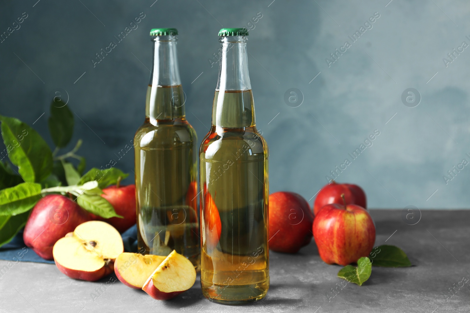 Photo of Delicious cider and apples with green leaves on gray table