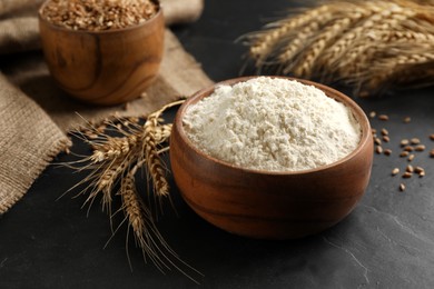 Wooden bowl of flour and wheat ears on black table