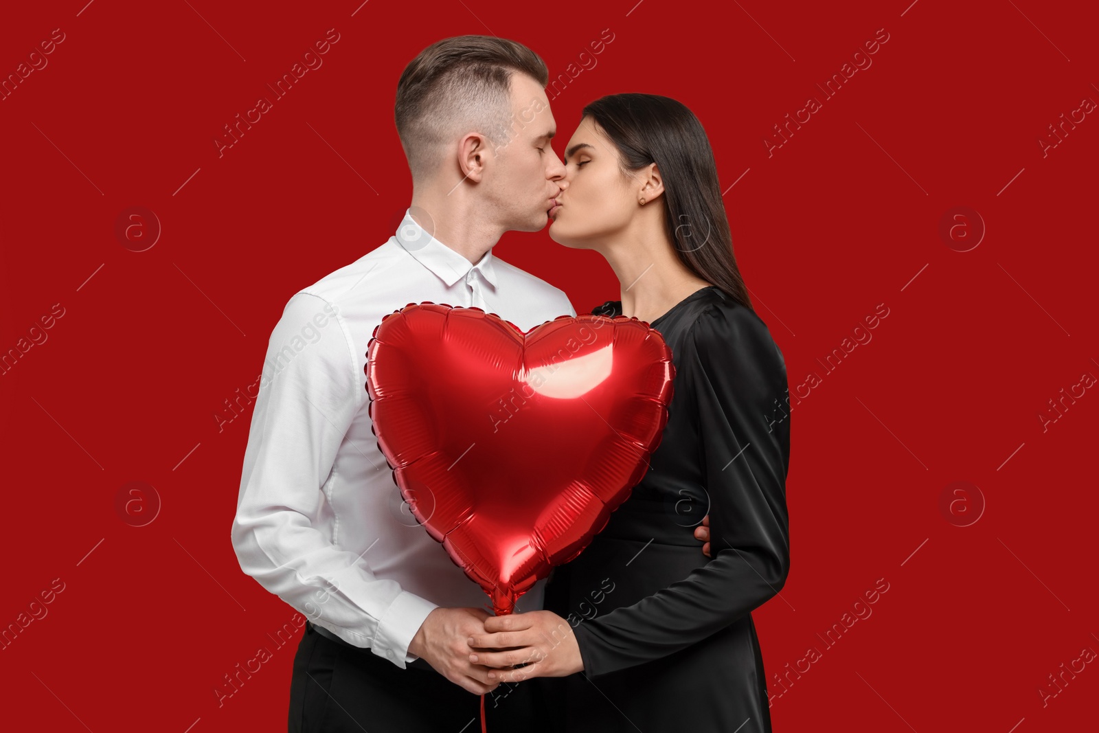 Photo of Lovely couple with heart shaped balloon kissing on red background. Valentine's day celebration