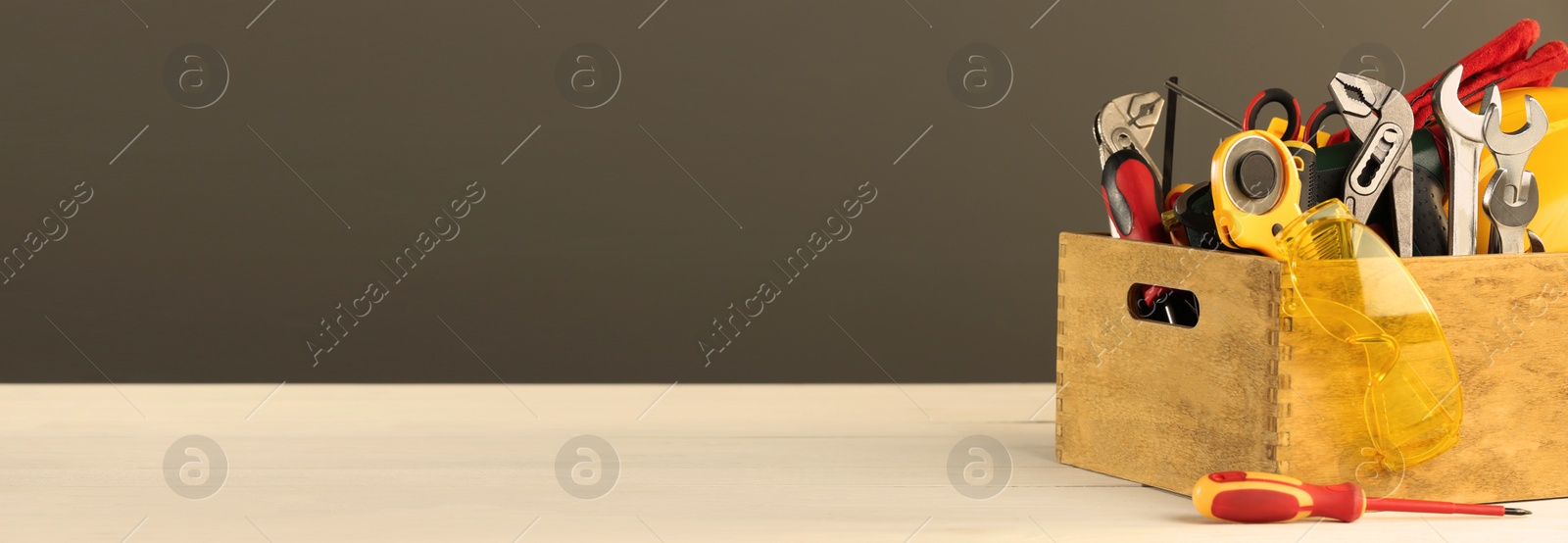 Image of Wooden box with different tools for repair on light wooden table, space for text. Banner design